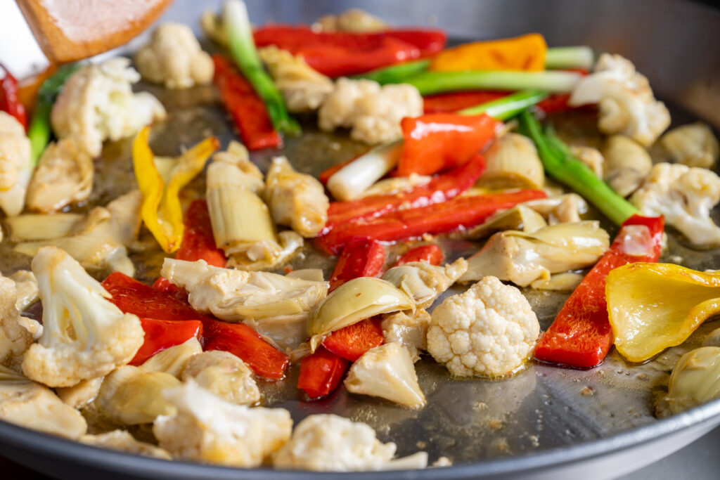 Artichokes, cauliflower, peppers and green onions sautéing in the paella pan
