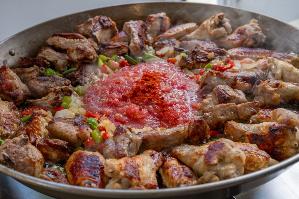 Sofrito with tomato and paprika over seared chicken and pork in the paella pan