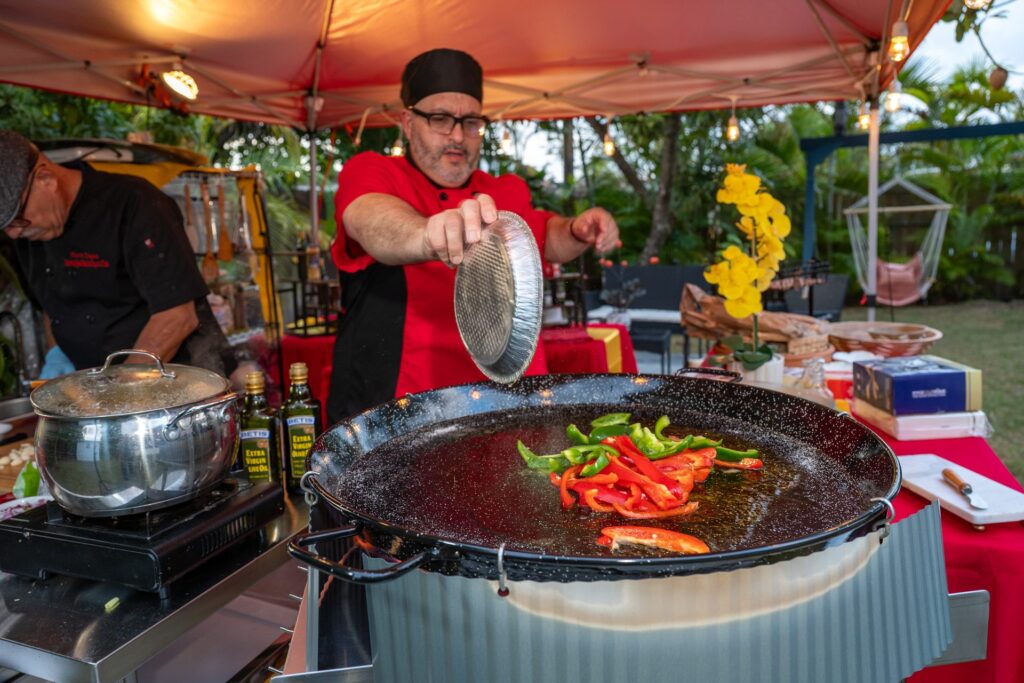 Chef Nino adding peppers to the paella pan under the pavilion